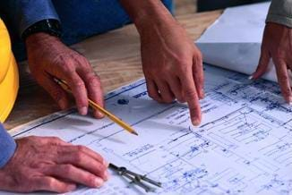 A photograph of architects pointing to (and discussing) a blueprint.