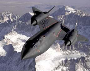 Photograph of the SR-71 Blackbird, a very fast, high-altitude airplane, shown flying high above a mountain landscape.