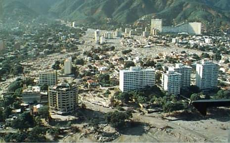 Aerial photo showing sediment pooling around roads, buildings and skyscrapers in a valley and alluvial fan below mountains.