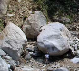 Photo of a man looking tiny standing next to a huge boulder.