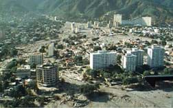 Aerial photo showing sediment poured around roads, buildings and skyscrapers in a valley and alluvial fan below mountains.