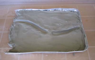 Baking pan filled with clay shaped into a slightly curved riverbed with a break at one point in the riverbed.