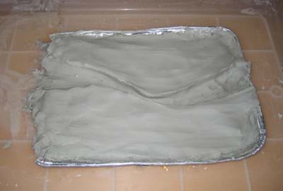 Baking pan filled with clay shaped into a curved and narrowing pathway.