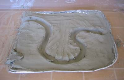 Baking pan filled with clay shaped into a riverbed with a large curve.