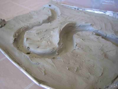 Baking pan filled with clay shaped into a riverbed with a large curve and a protective levee.