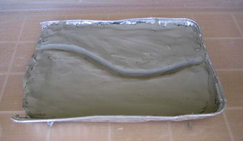 Baking pan filled with clay shaped into a slightly curved riverbed.