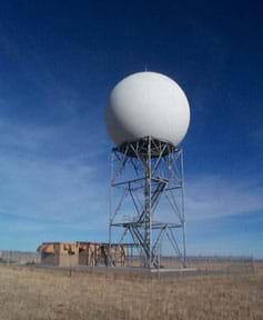 Photo shows a three-story metal tower with stairs to a large white sphere inside which the radar is housed.