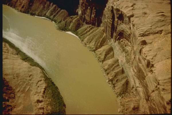 Aerial photo of a muddy brown stream running between two cliffs.
