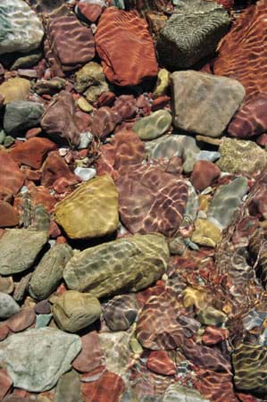 Photo shows different colored rocks through the clear water of a stream.