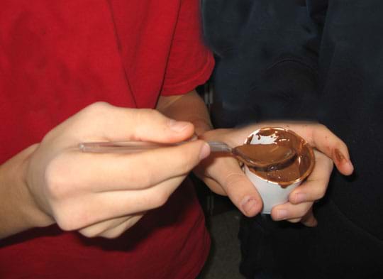 Photo shows hands holding a small cup of melted chocolate.