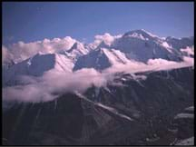 Photo shows a mountain range in the clouds with snow-covered peaks.