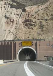 Photo shows view from a highway looking into an arched tunnel entrance cut into the rock face of a mountain.