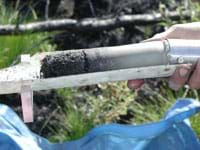 Photo shows a hand holding a smooth, tube-shaped chunk of soil, resting in a metal holder.