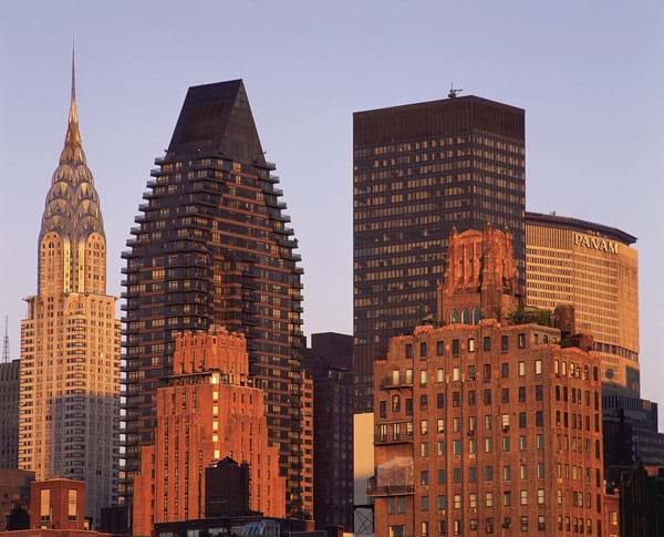 Photograph of pyramid-shaped tops of skyscrapers in orange light of sunset.