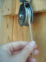 Photograph of a hand-sized metal pulley with string run over the wheel.