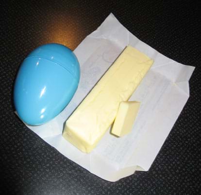 Photo shows blue plastic egg and stick of butter with one slice cut off.