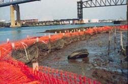 An orange plastic fence and post system holds back junk and sediment from entering a larger body of water.