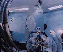 Photo shows three technicians in white clean room garb delicately working on a huge shiny vertical surface.