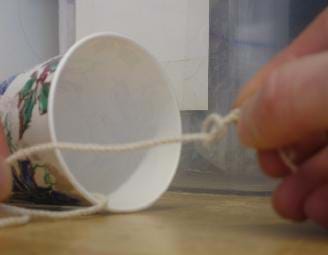 Photo shows a paper cup tipped sideways showing a piece of string threaded through the bottom.