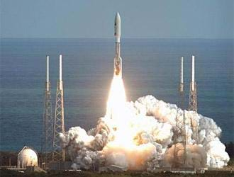 Photo shows a silver rocket at liftoff with flames coming out the bottom of the rocket and clouds of combustion below.