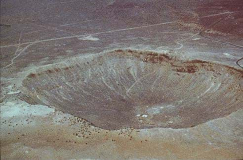 Aerial photo shows expanse of dry earth with some roads, with a very large bowl-shaped depression into the ground surface.