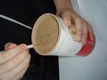 A student cuts a hole in the bottom of the oatmeal container using an Exact-o knife.