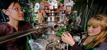 Two young women work on a intriguing machine made of metal parts.