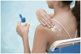 A photograph shows a girl in bathing suit reaching over her shoulder to put a white cream (sunscreen) on her back.