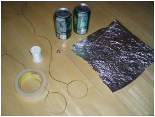 Photo shows two soda cans, tape, spool of thread, aluminum foil, bell and copper wire on a tabletop.