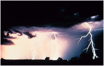 Photo shows a dark, cloudy night sky lit up by many lightning strikes.