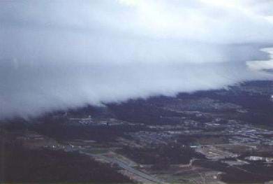 A photo shows bank of very thick, layered white clouds above a town.