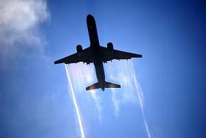 A Boeing 757-300 airplane flying in the sky making sheets of condensation.
