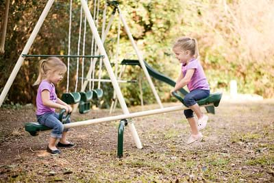 two young girls sitting on a seesaw.