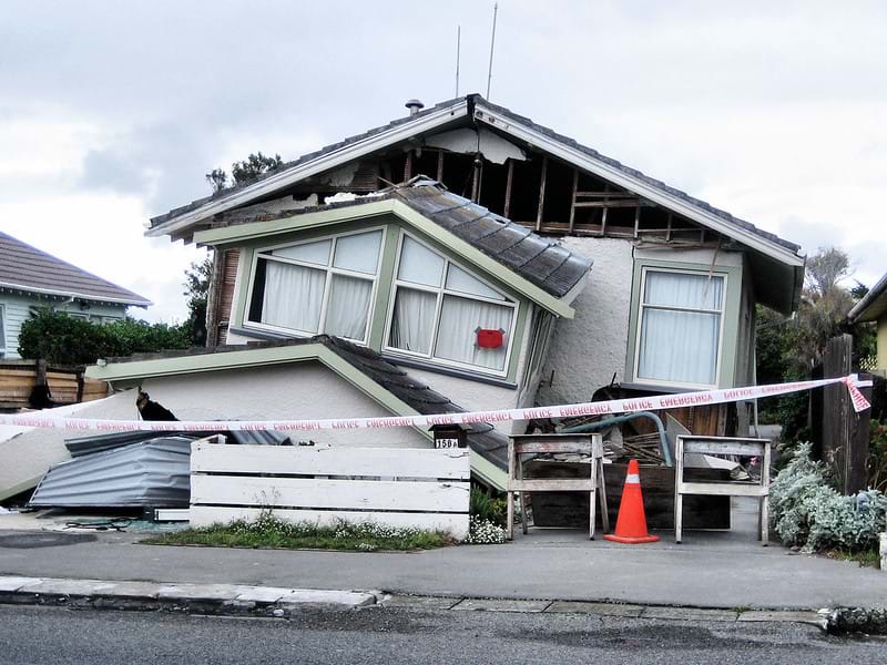 A picture of a house damaged by an earthquake. The front porch of the house appears to be lopsided and ready to fall over.