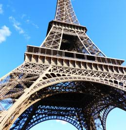 A photograph shows a large, tall and pointed exposed steel truss structure that has four legs on the ground that rise and merge into one tall tapered tower.