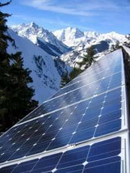 Photo shows sun reflecting off shiny blue roof panels with snowcapped mountains in background.