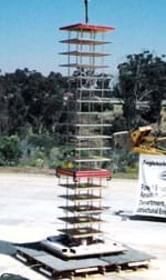 Photo shows a tall tower made of platforms and columns placed on a wider base located in an open parking lot.