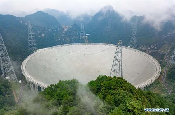 Photo shows a huge dish inset into a forested valley, with structures and towers around it.