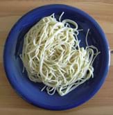 A photo from above shows an entwined mass of cooked (soft), white spaghetti noodles (long) in a blue bowl.