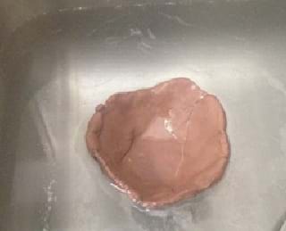 A photograph shows a piece of clay, flattened and rounded, floating in water.