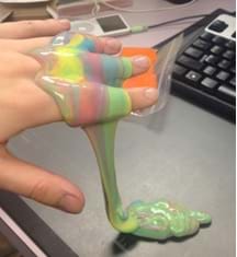 A photograph shows a hand with multi-colored silly putty dripping off it. 
