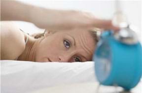 A photograph shows a woman waking up and reaching for an alarm clock near her bed.