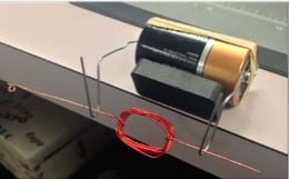 La fotografía muestra un dispositivo compuesto de una pila D, imán, goma elástica, dos clips y una bobina de alambre rojo.