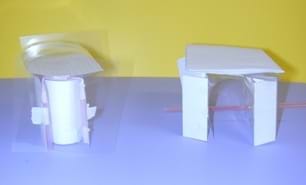 A photograph shows two building structures made of folded and taped paper and plastic.