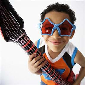 A photograph of a kid wearing funny glasses and holding the neck of a six-stringed acoustic guitar.