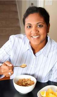 A photograph shows a woman at a table taking a bite of cereal from a bowl.