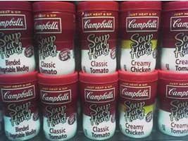 Photograph of 10 Campbells soup cans with plastic lids on a grocery store shelf.