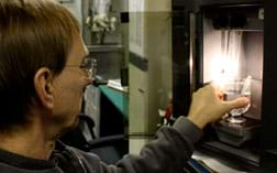 Photo shows a man putting a beaker and test tube of clear fluids into a black, box-shaped desktop appliance.