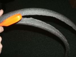 Photo shows a hand and scissors cutting a tube of insulation foam in half lengthwise to make two tracks.