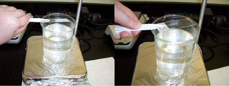 Two photos, both show a hand holding a glass slide over a cup of water on a hot plate: (left) The glass slide is foggy. (right) The glass slide is nearly clear.